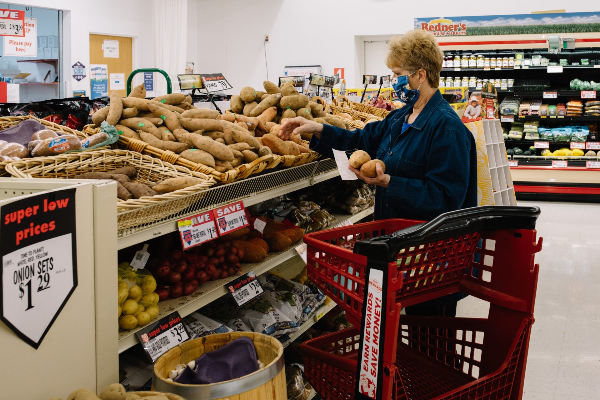 A shopper wearing a fabric mask picks out potatoes at the grocery store on April 10, 2020.