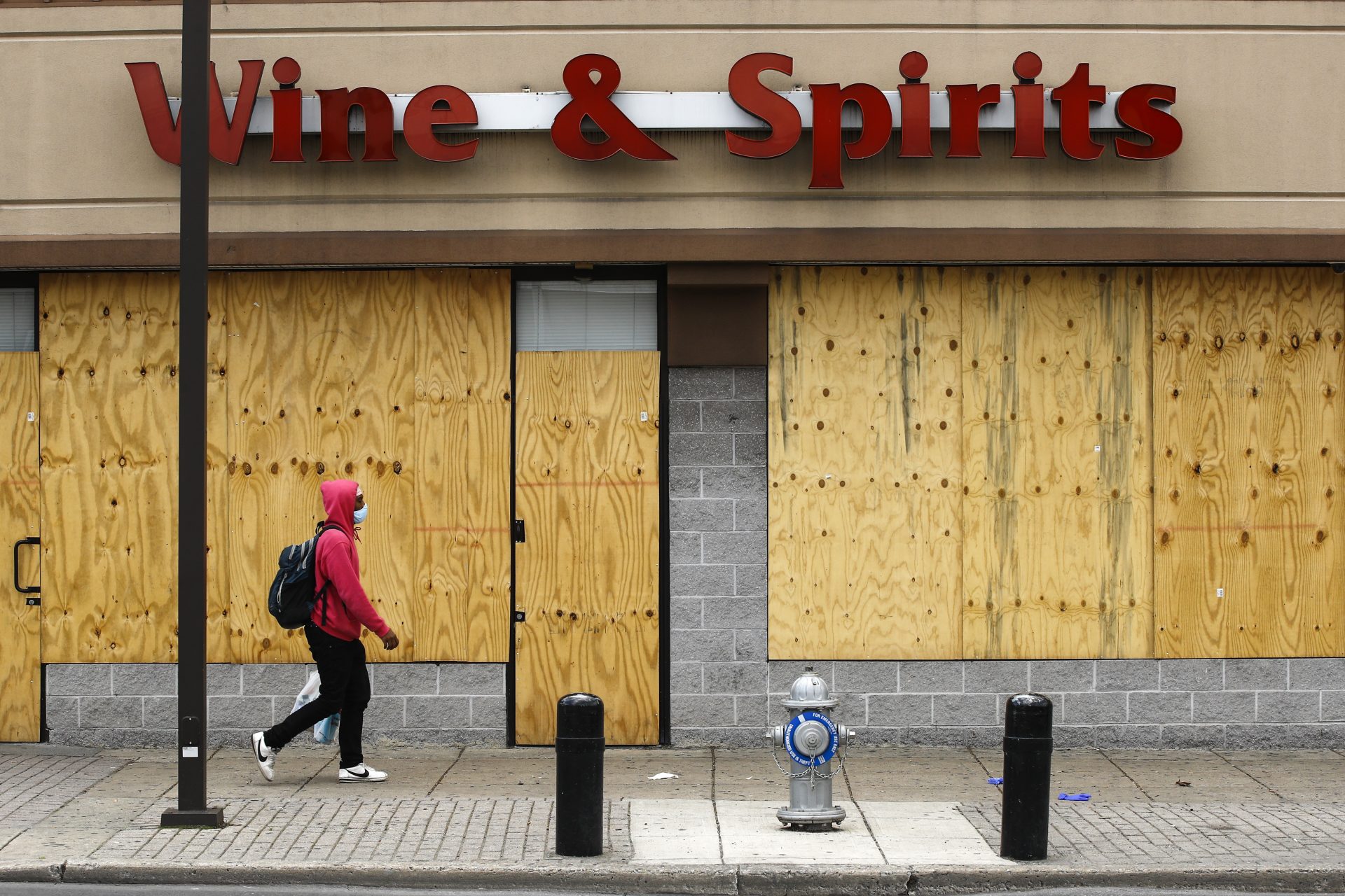 A person wearing a protective face mask as a precaution against the coronavirus walks past a boarded up Wine and Spirits store in Philadelphia, Thursday, April 16, 2020. Pennsylvania's liquor agency says workers are coming back on the job at more than 100 shuttered state-owned liquor stores to help process online orders.