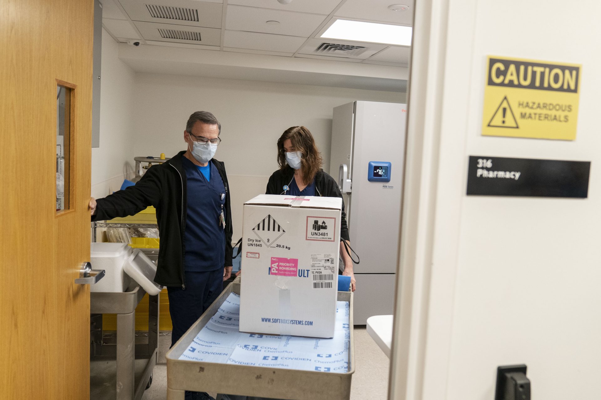 Pharmacists Richard Emery, left, and Karen Nolan, wheel a box containing the Pfizer-BioNTech COVID-19 vaccine next to a storage freezer as it arrives at Rhode Island Hospital in Providence, R.I, Monday, Dec. 14, 2020.