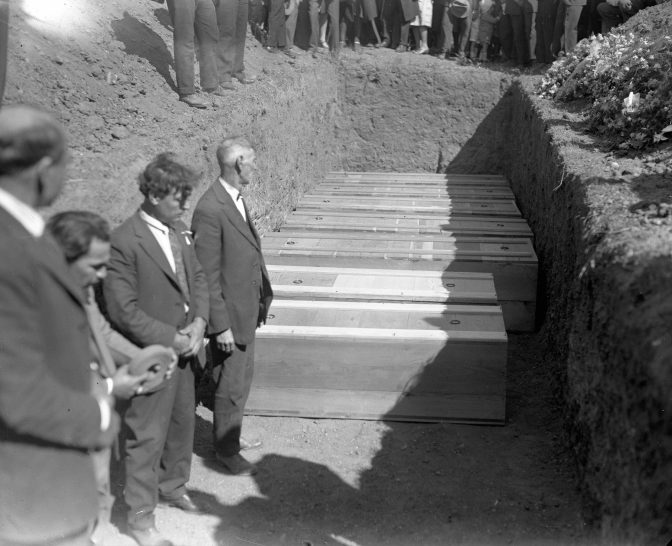 Men standing near coffins in a dug out trench.