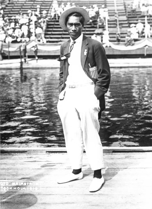 A man in white and a dark jacket stands in front of a body of water
