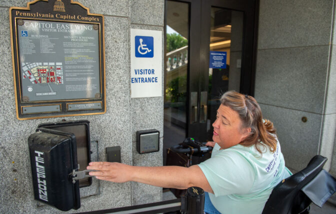 Pam Auer, director of advocacy at Center for Independent Living of Central Pennsylvania, reaches for the phone used to call Capitol Police at the East Wing entrance to the Pennsylvania Capitol complex in Harrisburg Tuesday, June 4, 2024. According to Auer, on weekends and holidays, people with physical disabilities need to call Capitol Police to access the complex. This entrance is the only entrance to the capitol that can be entered using a wheelchairs of scooter.