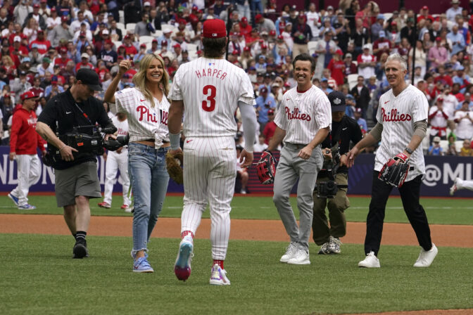 FILE - Kaitlin Olson, left, Rob McElhenney, second from right, and former Philadelphia Phillies second baseman Chase Utley, right, participate in opening ceremonies before the start of a baseball game between the New York Mets and the Philadelphia Phillies at London Stadium, in London, Sunday, June 9, 2024. McElhenney keeps an eye on the Phillies no matter how far away he is filming TV shows or leading his Wrexham soccer team. He even goofed around with the Phillies on their recent trip to London.(AP Photo/Vera Nieuwenhuis, File)